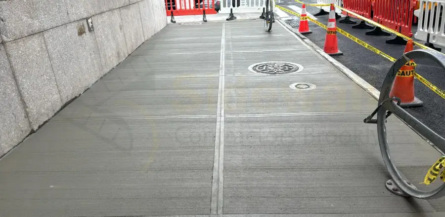 Newly finished concrete sidewalk with a utility cover outside a commercial building