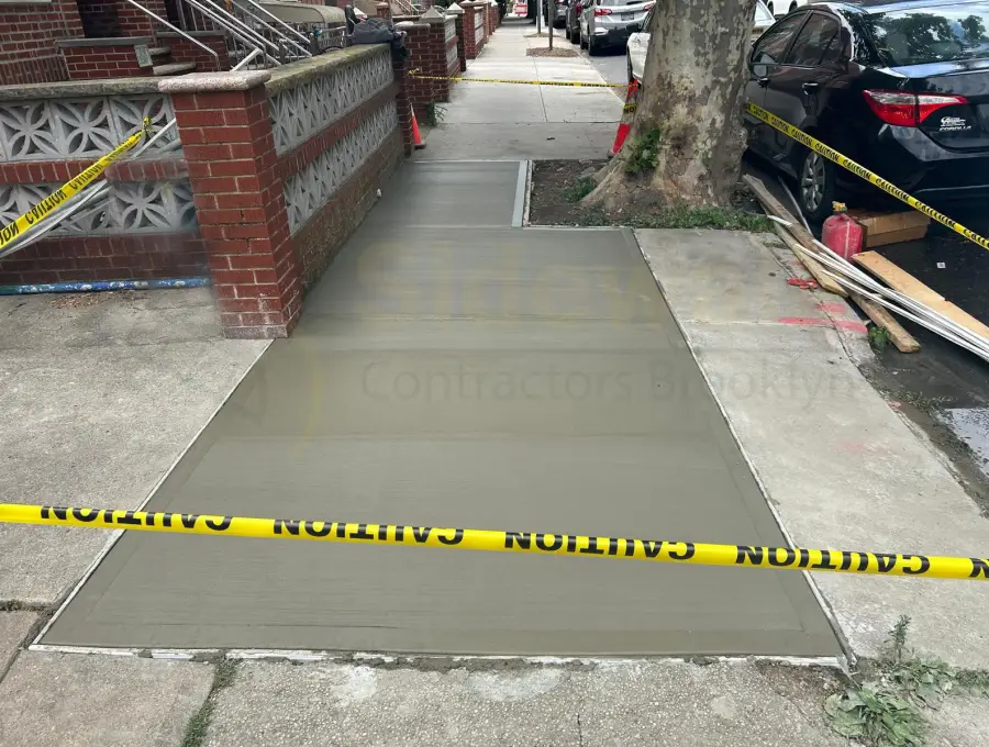 Freshly poured sidewalk flag between a brick wall and a street tree, taped off while it cures